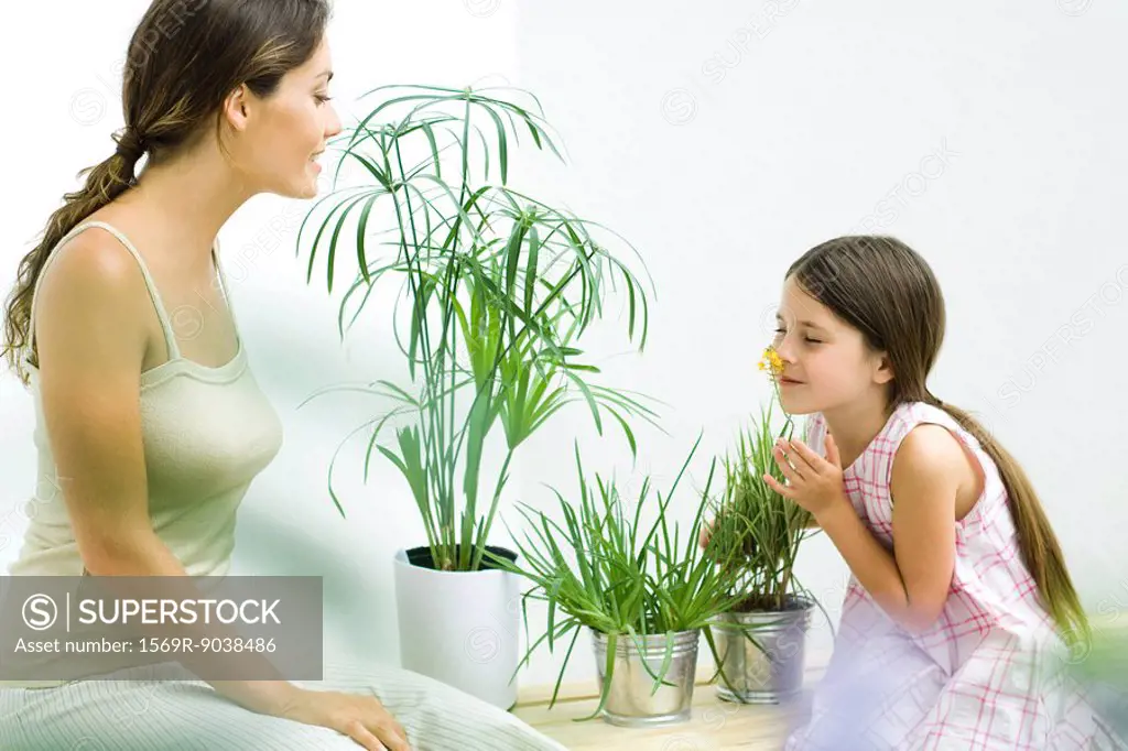 Mother and daughter sitting with potted plants, girl smelling flower, eyes closed