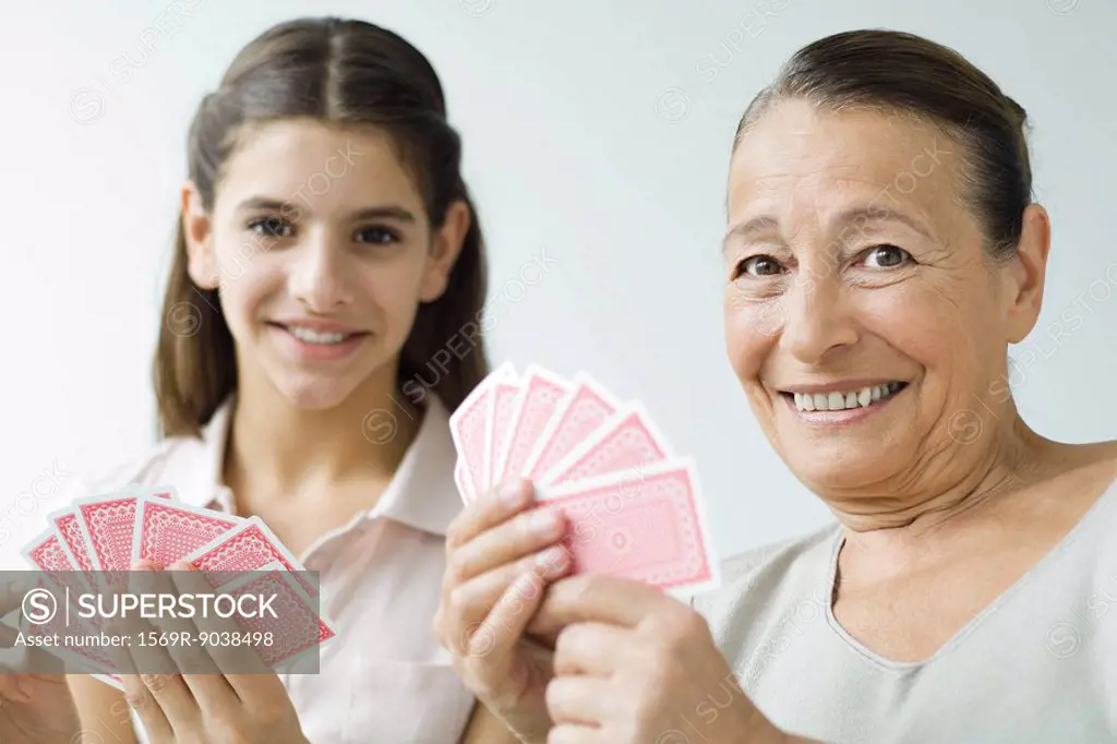 Grandmother and granddaughter playing cards, smiling at camera