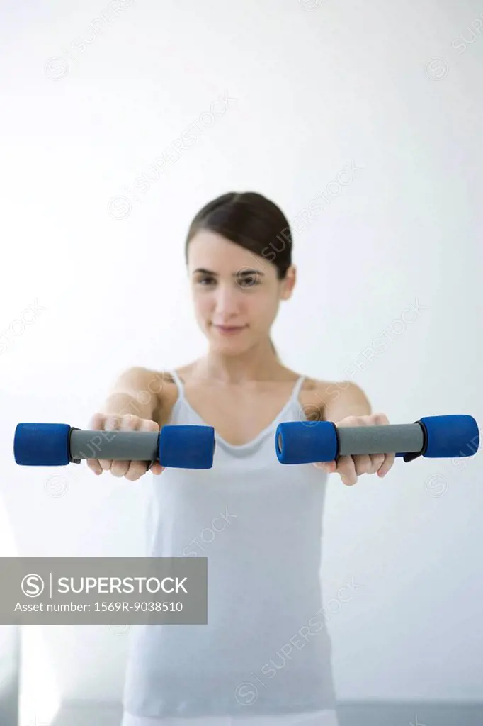 Young woman holding out pair of dumbbells, smiling at camera