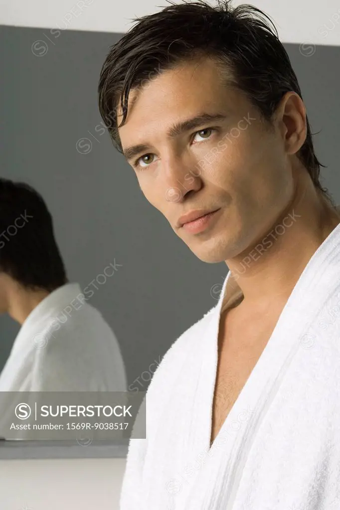 Man wearing bathrobe, looking away, mirror in background