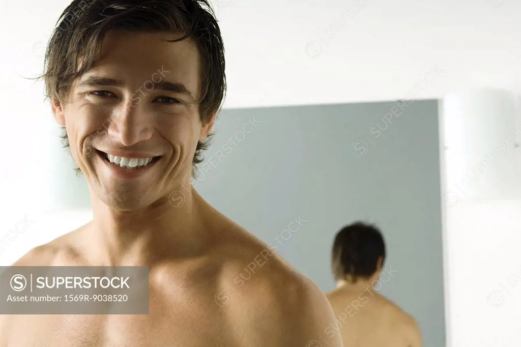 Bare-chested man smiling at camera, mirror in background, portrait