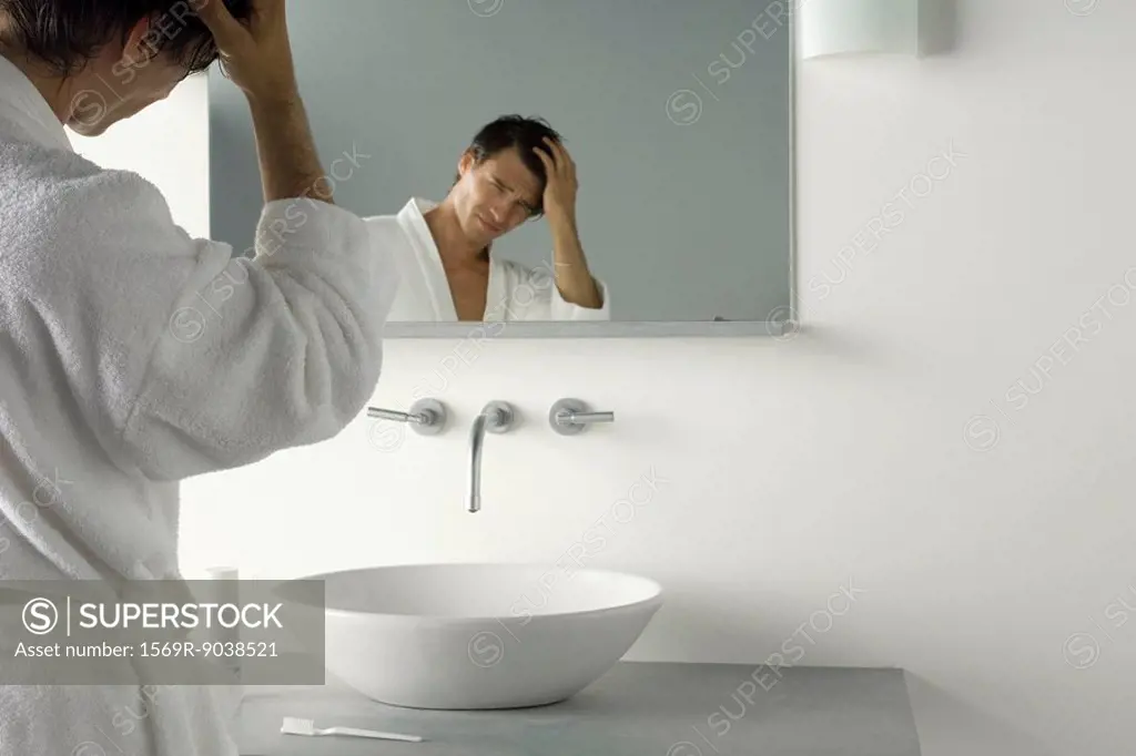 Man holding head, frowning at himself in mirror