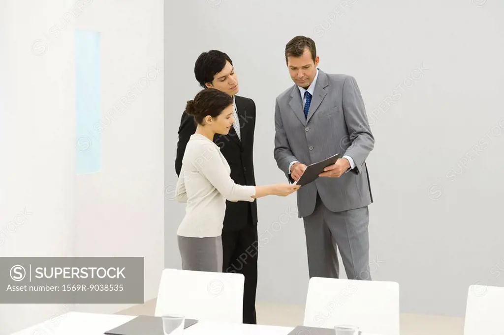 Professionals standing in conference room, looking down at folder
