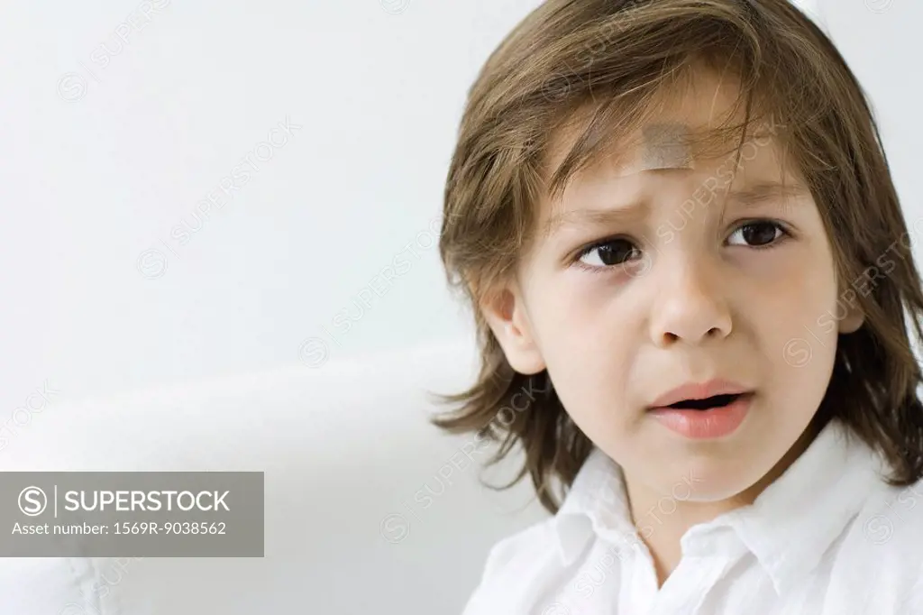 Little boy with adhesive bandage on his forehead, looking away and furrowing brow
