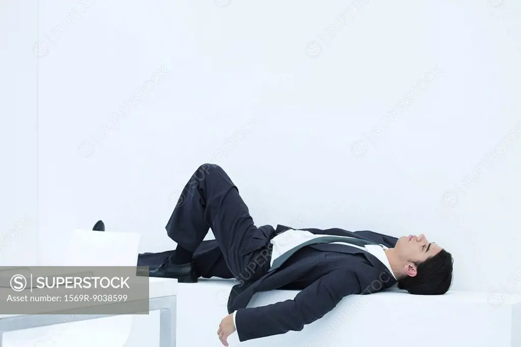 Businessman lying down on ledge in office