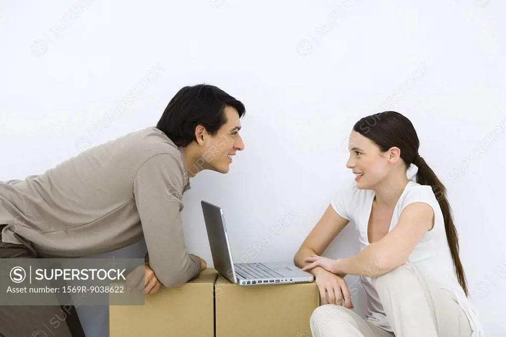 Couple sitting at makeshift desk with laptop computer between them, smiling at each other