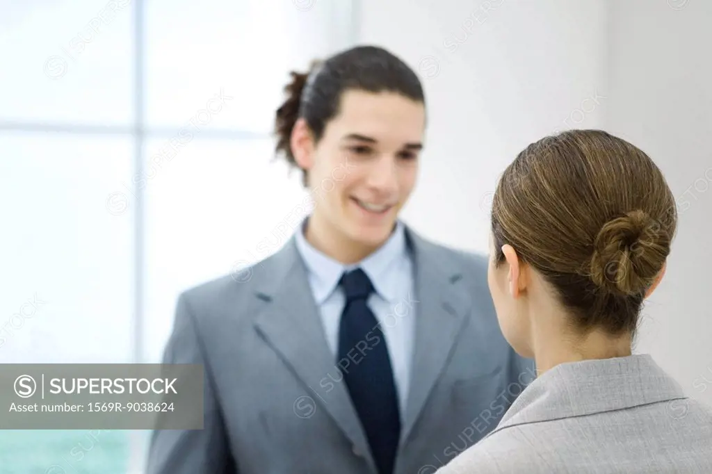 Professional young man facing female colleague, smiling
