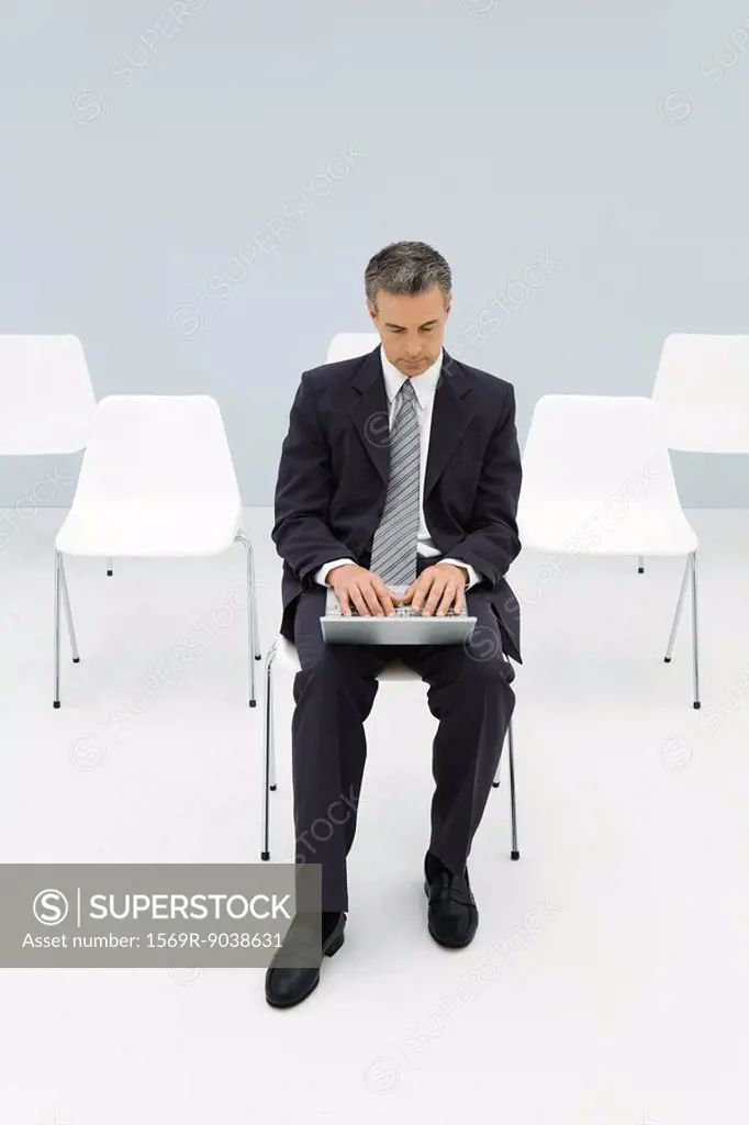 Businessman sitting in chair using laptop, empty chairs in background