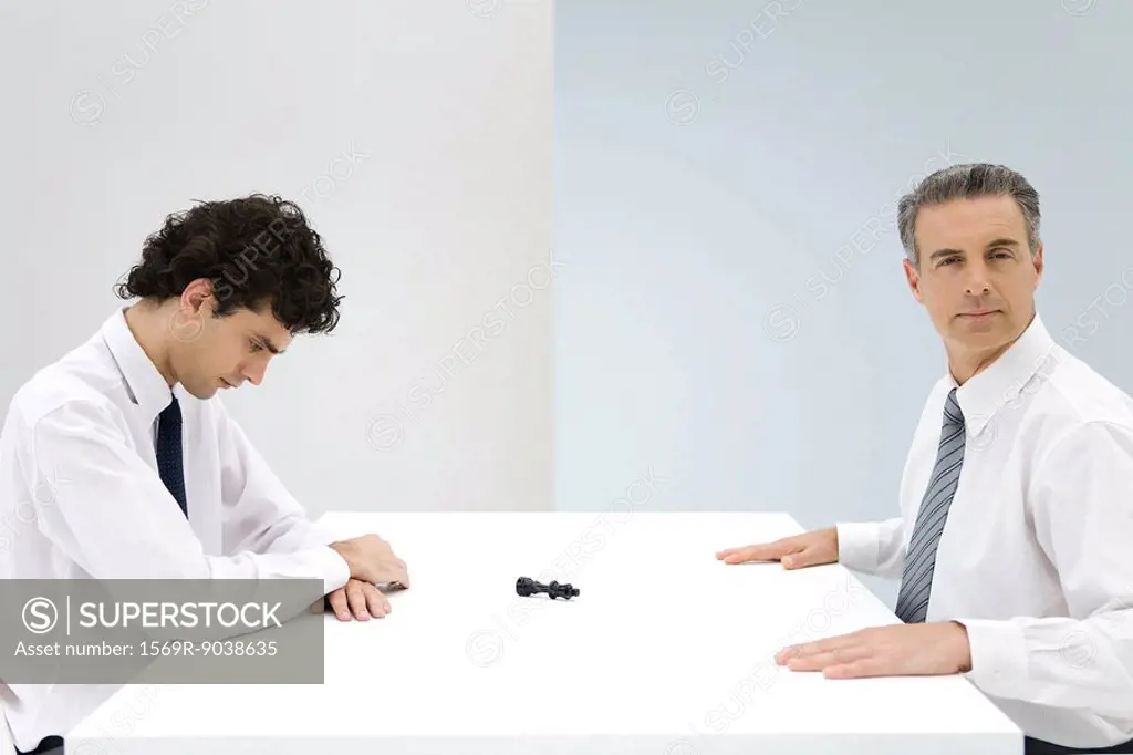 Businessmen sitting at table, tipped over chess piece between them