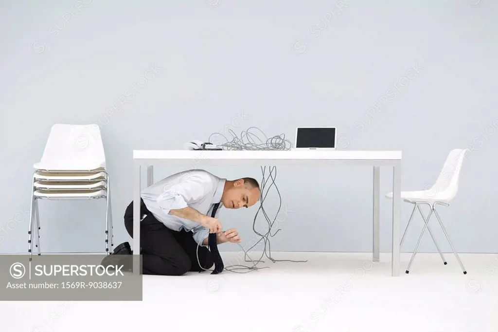 Businessman kneeling under table, examining cords