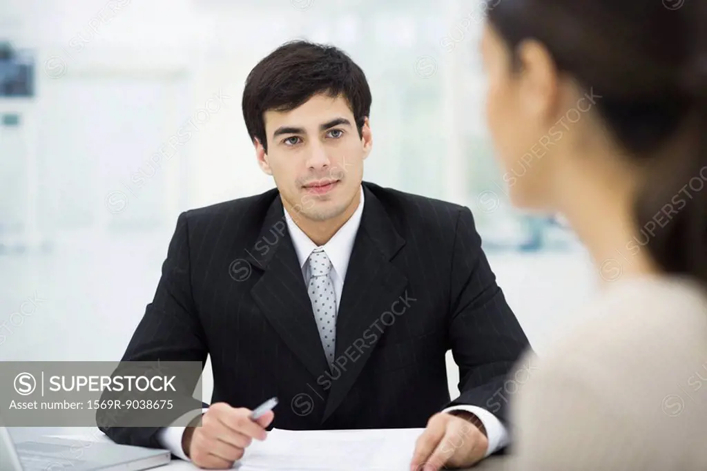 Businessman sitting at desk, listening to female client