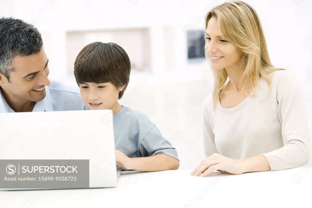 Father and son using laptop computer together, mother watching