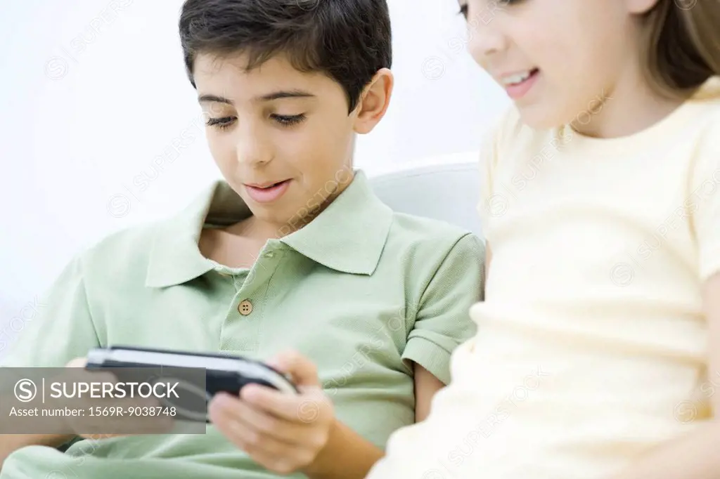 Brother and sister sitting together, boy playing handheld video game