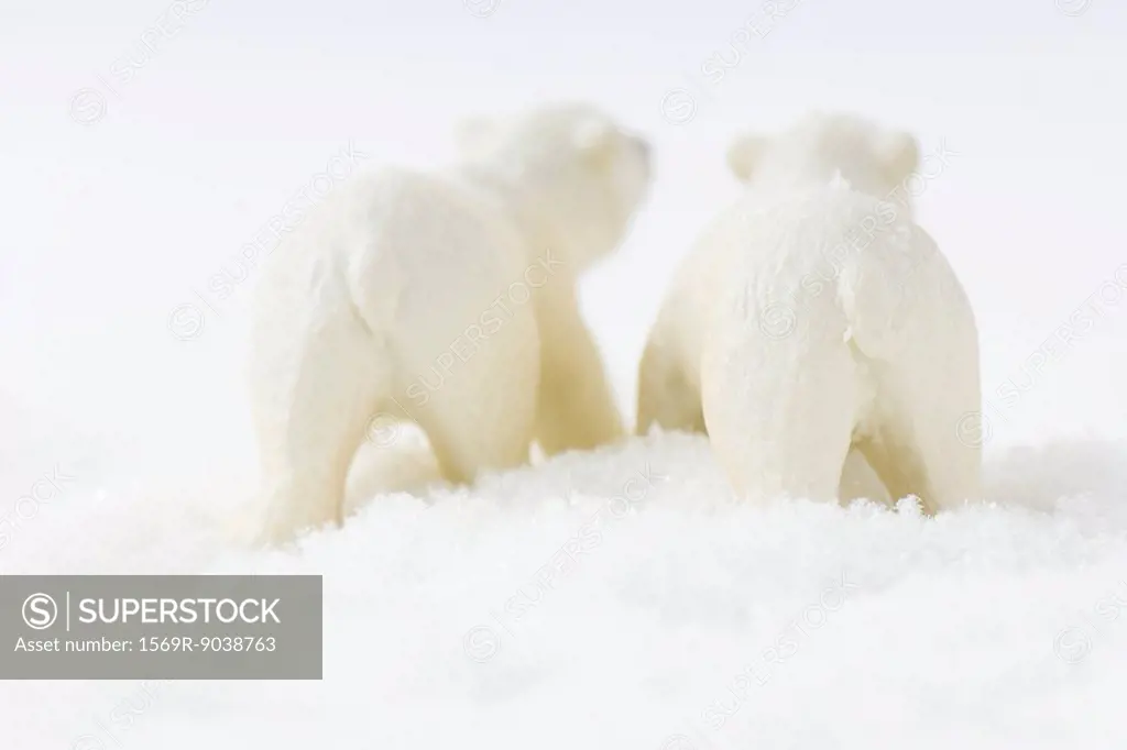 Two toy polar bears walking in snow, rear view