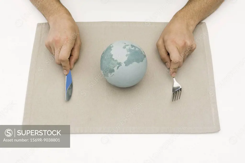 Person sitting before globe on placemat, holding fork and knife, cropped view