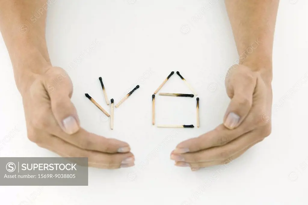 Hands protecting burnt matches arranged in shape of house and tree