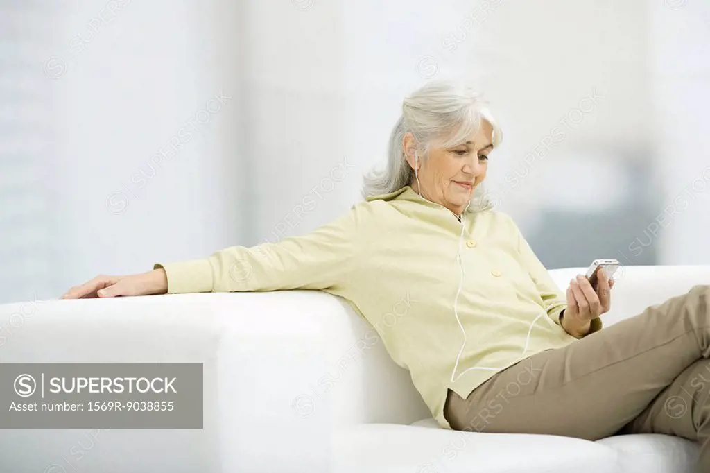 Senior woman listening to MP3 player, sitting on couch