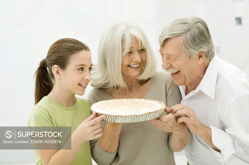 Grandparents and granddaughter smiling at each other, woman holding pie