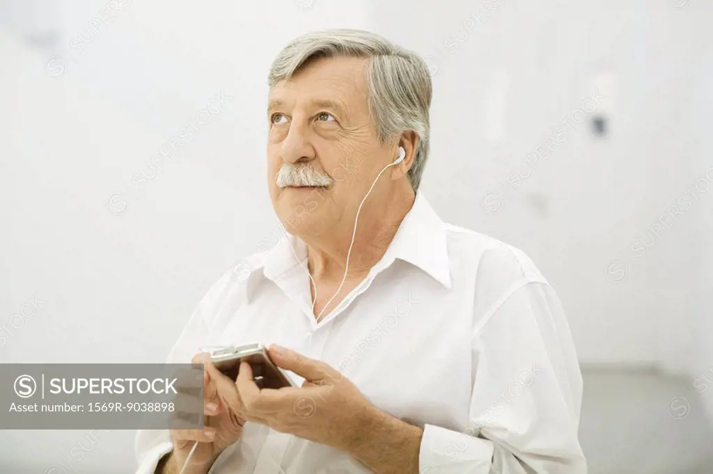 Senior man listening to MP3 player, looking up