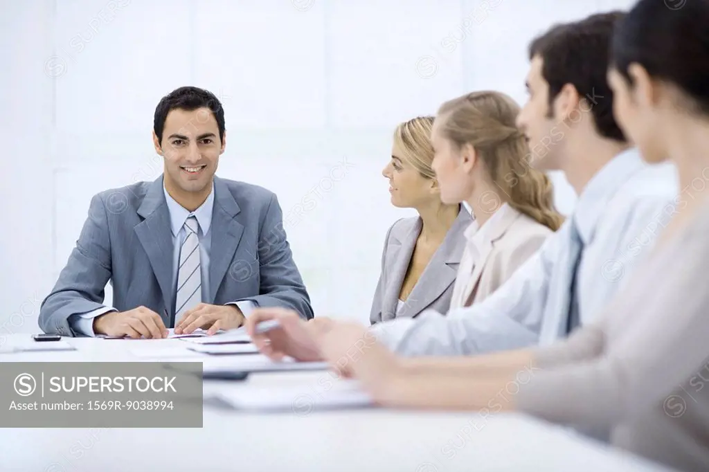 Businessman sitting with colleagues at conference table, smiling at camera