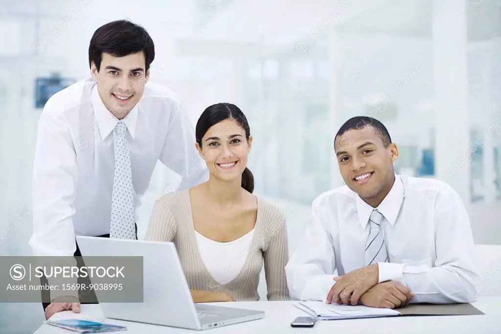 Professionals gathered around laptop computer, smiling at camera