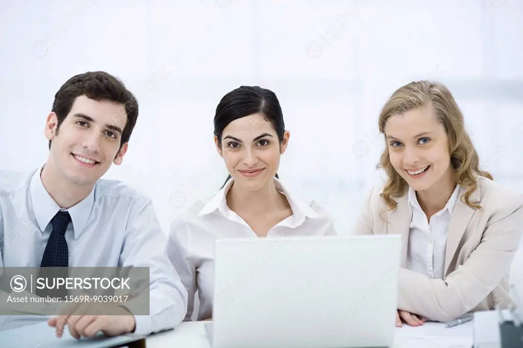 Team of professionals sitting with laptop computer, smiling at camera