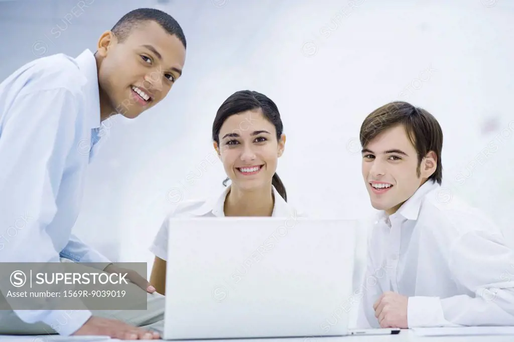Young professionals gathered around laptop computer, smiling at camera