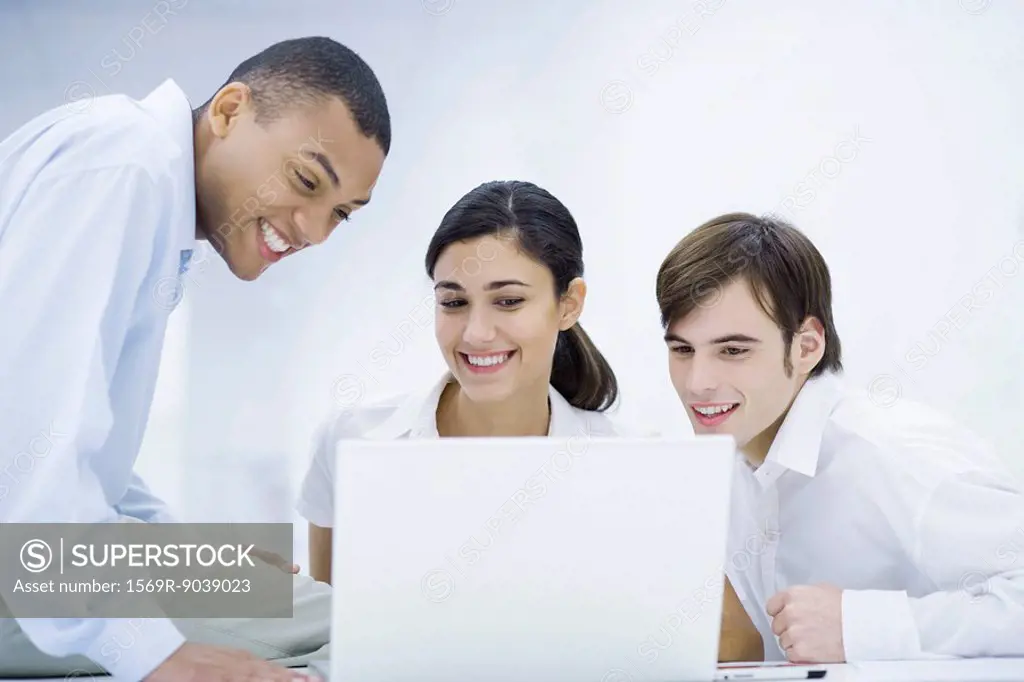 Young professionals looking at laptop computer together, smiling
