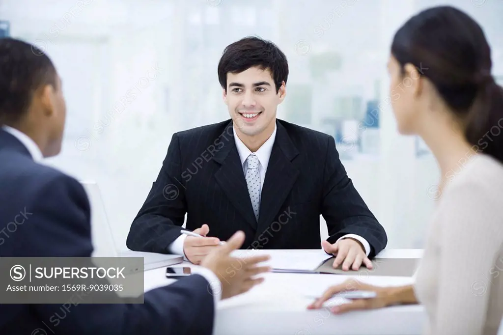 Businessman sitting at desk, talking with clients and smiling