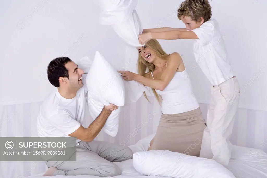 Parents and young son having pillow fight on bed