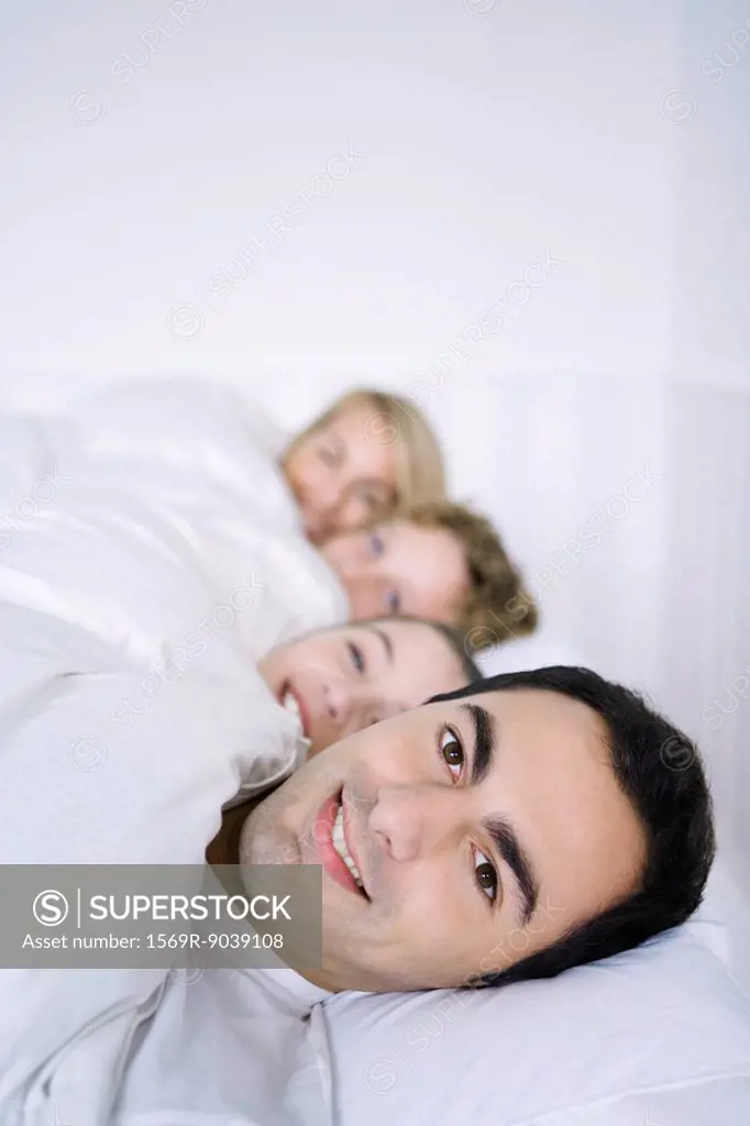 Man lying in bed with his family, smiling at camera