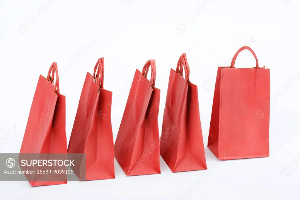 Five red shopping bags arranged side by side, one turned at right angle to others