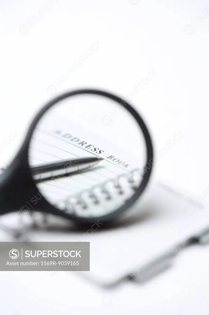 Magnifying glass over address book and pen, close-up
