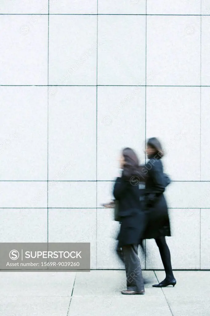 Two businesswomen walking side by side down sidewalk