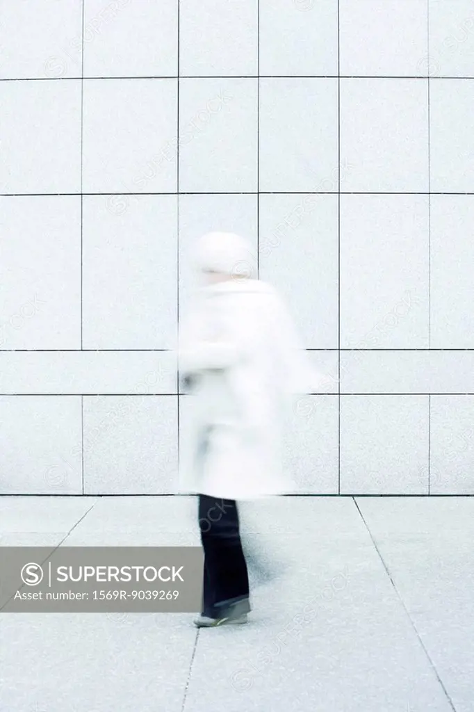 Woman wearing white coat, white knit hat and white knit scarf walking down sidewalk