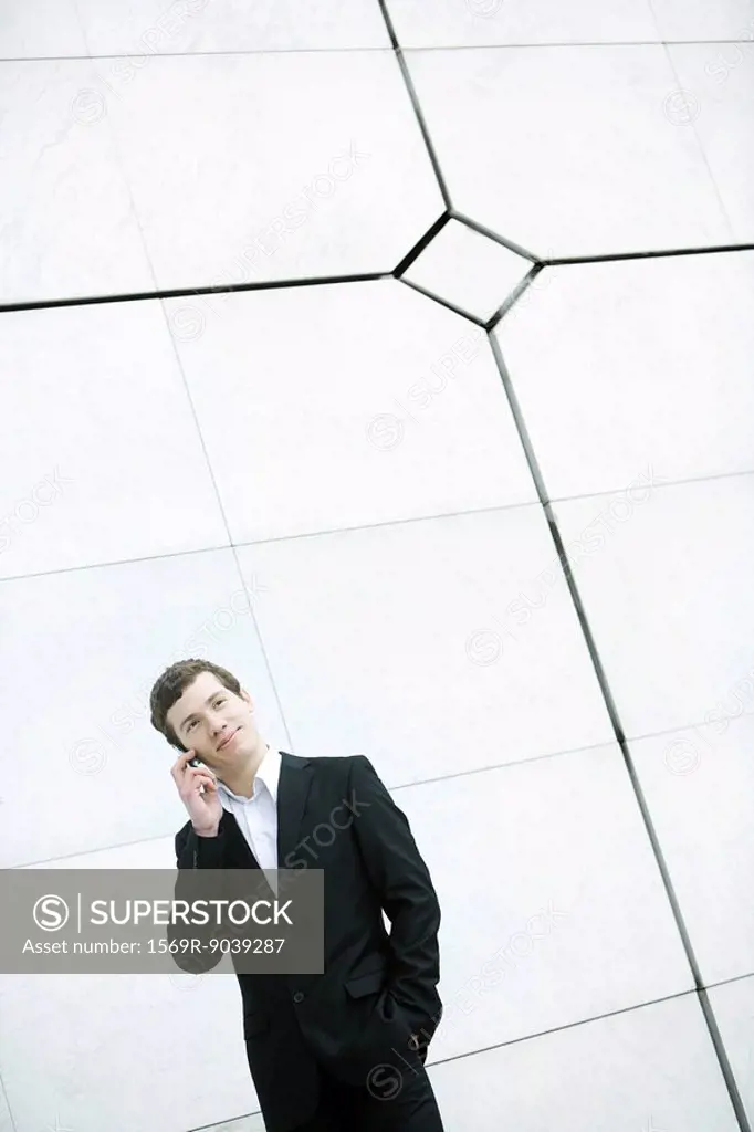 Businessman using cell phone, hand in pocket, casually standing by wall