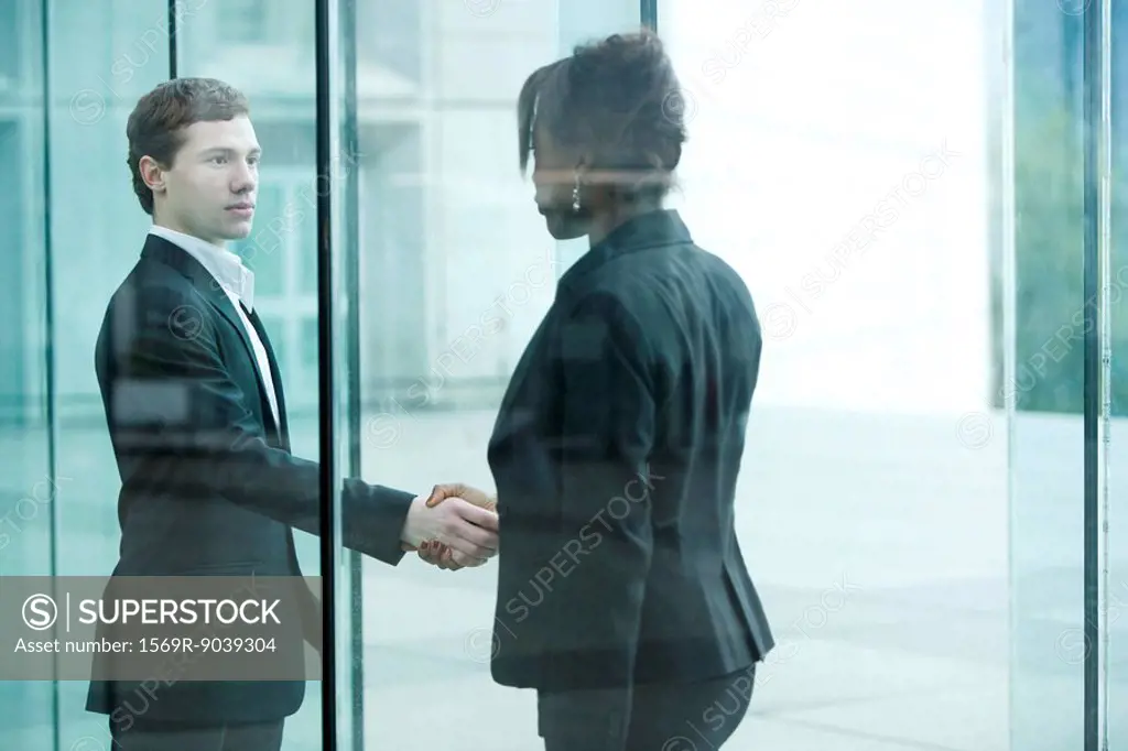 Businessman and businesswoman meet and shake hands at building entrance