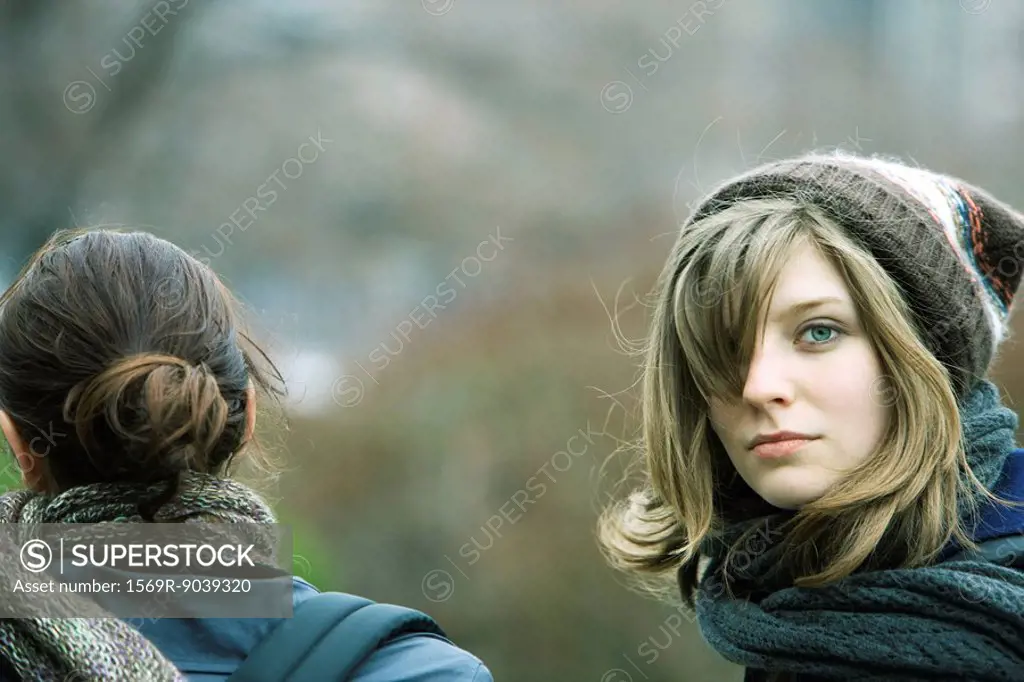Young woman walking with friend in park, looking over shoulder at camera