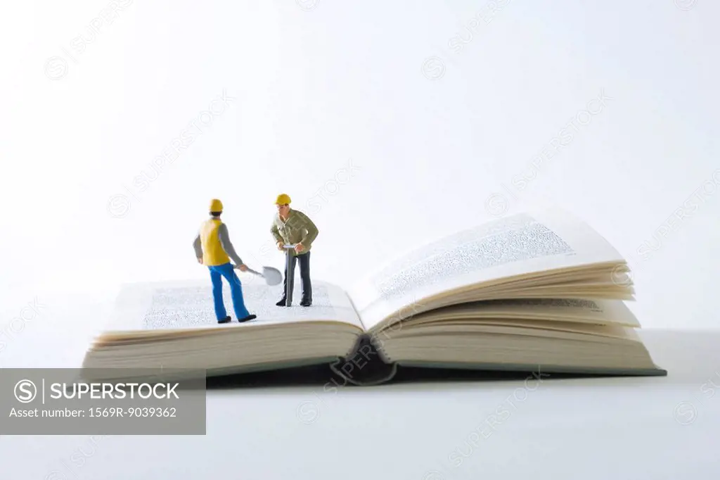 Miniature construction workers standing on open book
