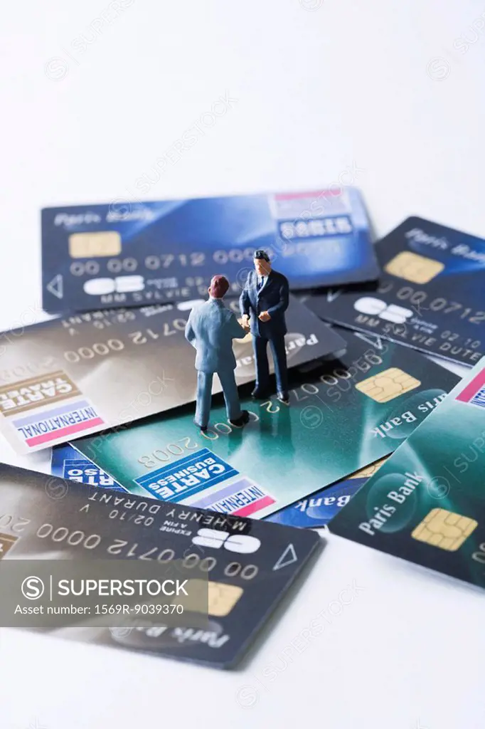 Miniature businessmen shaking hands on pile of credit cards
