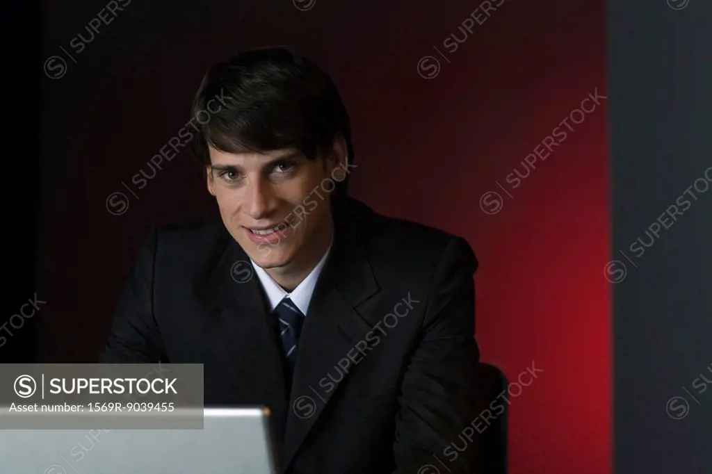Businessman smiling at camera over laptop, portrait