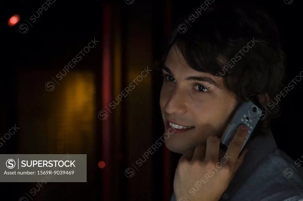 Man using cell phone, listening, smiling, looking away