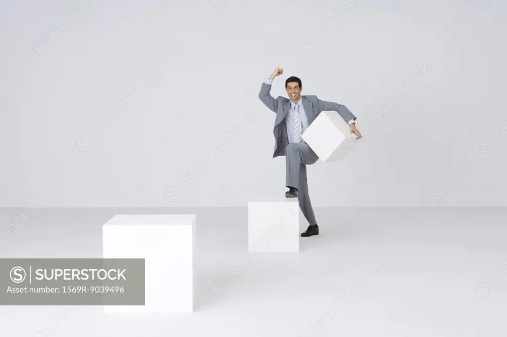 Businessman carrying block, stepping onto larger block