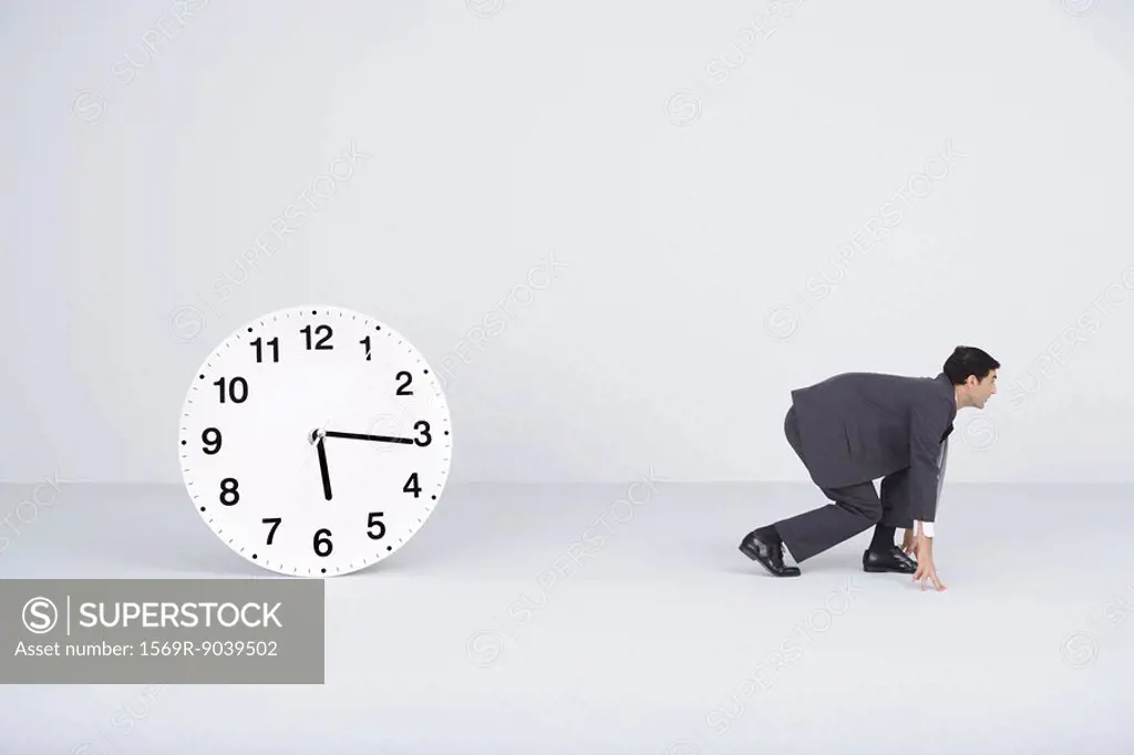 Businessman crouching, ready to run, next to clock