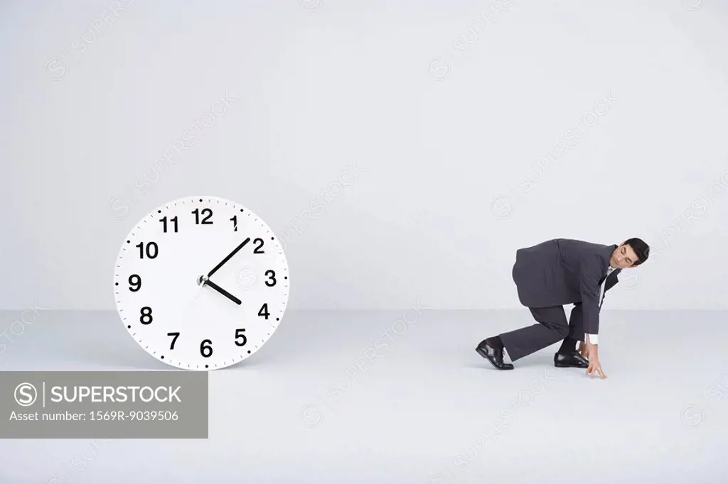 Businessman racing against time, looking over shoulder at large clock
