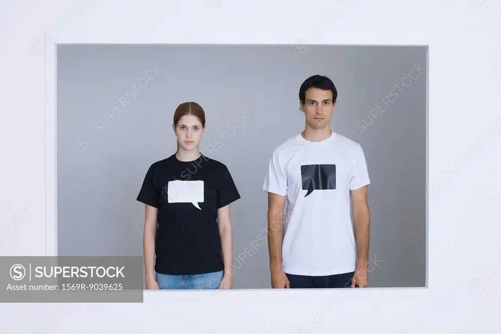 Young man and young woman wearing tee-shirts printed with blank word bubbles, looking at camera