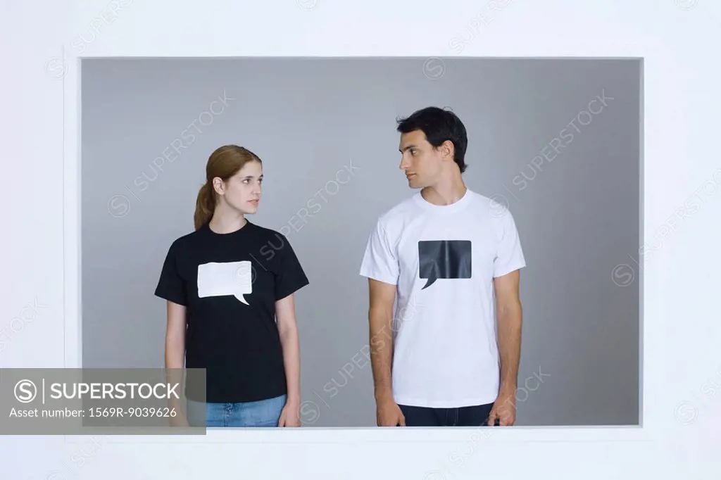 Young man and young woman wearing tee-shirts printed with blank word bubbles, looking at each other