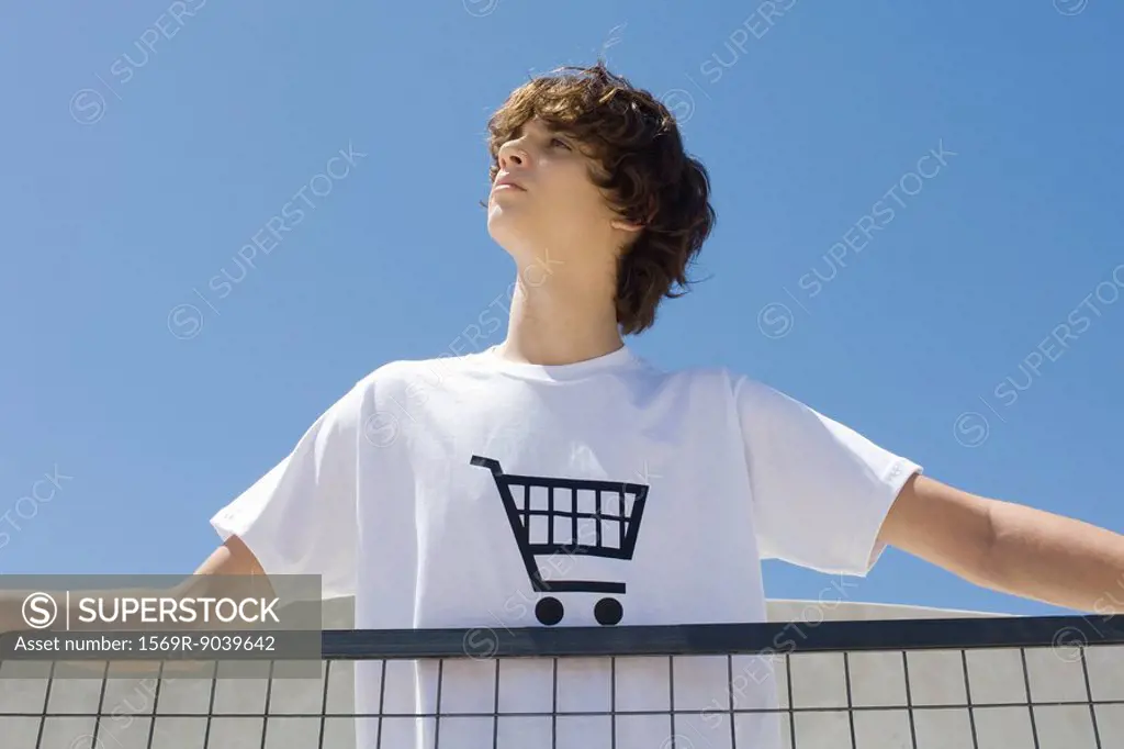 Teenage boy wearing tee-shirt printed with shopping cart, standing at railing, looking up