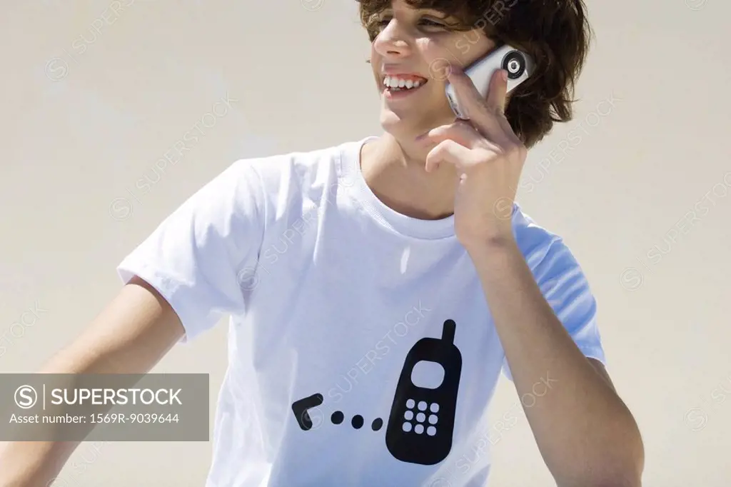 Teenage boy wearing tee-shirt printed with cell phone graphic, using cell phone, smiling