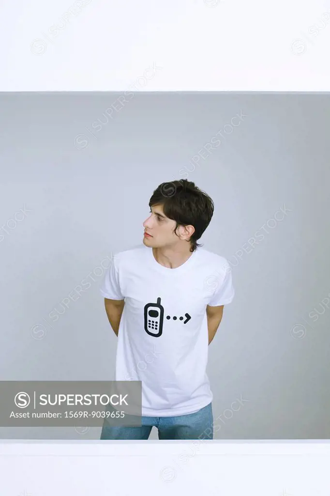 Young man wearing tee-shirt with cell phone graphic, looking away, hands behind back
